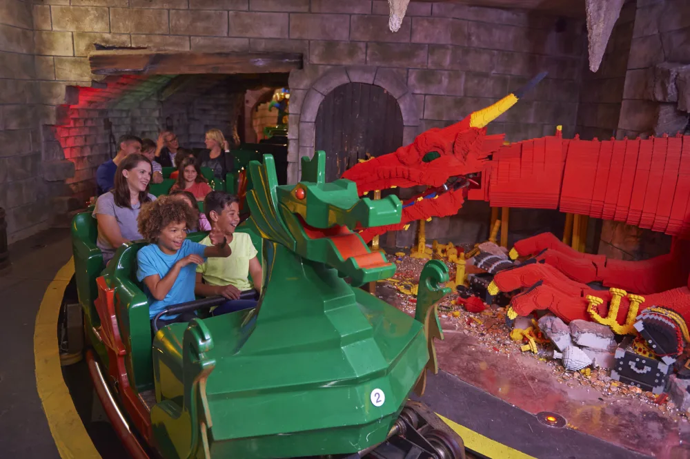 A carriage of people pass a large red Lego dragon on a ride at LEGOLAND Windsor