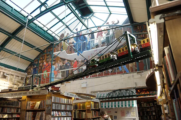 Interior of a bookshop with a glass roof and a model train hanging above the shelves